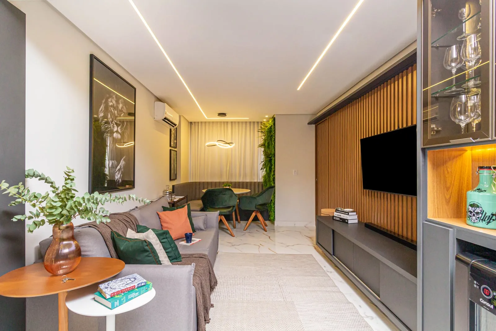 Sala de estar integrada com painel ripado, jardim vertical e mesa de refeições ao fundo.